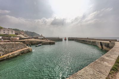 Harbor in sea against cloudy sky