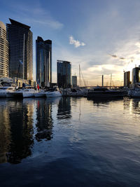 Sailboats moored on sea by buildings against sky in city