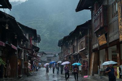 People with umbrella walking on street amidst buildings during rainy season