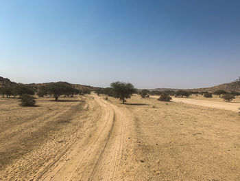 Dirt road amidst land against clear sky