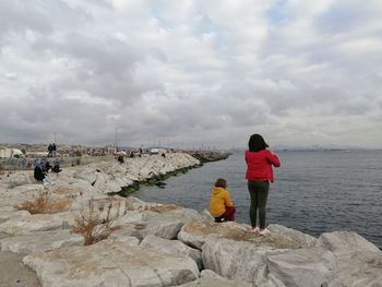 Rear view of people walking on beach against sky