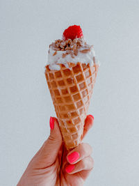 Hand holding ice cream cone against white background