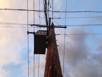 Low angle view of electricity pylon against cloudy sky