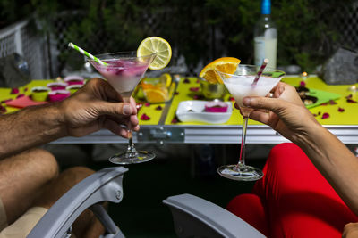 Happy romantic couple celebrating, holding glasses of cocktails with fruits and drinking straws. 