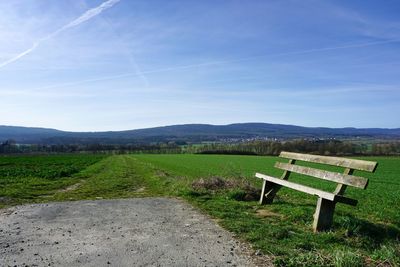 Empty bench on field against sky