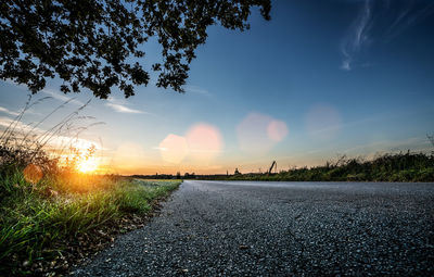 Road amidst trees on field against sky at sunset