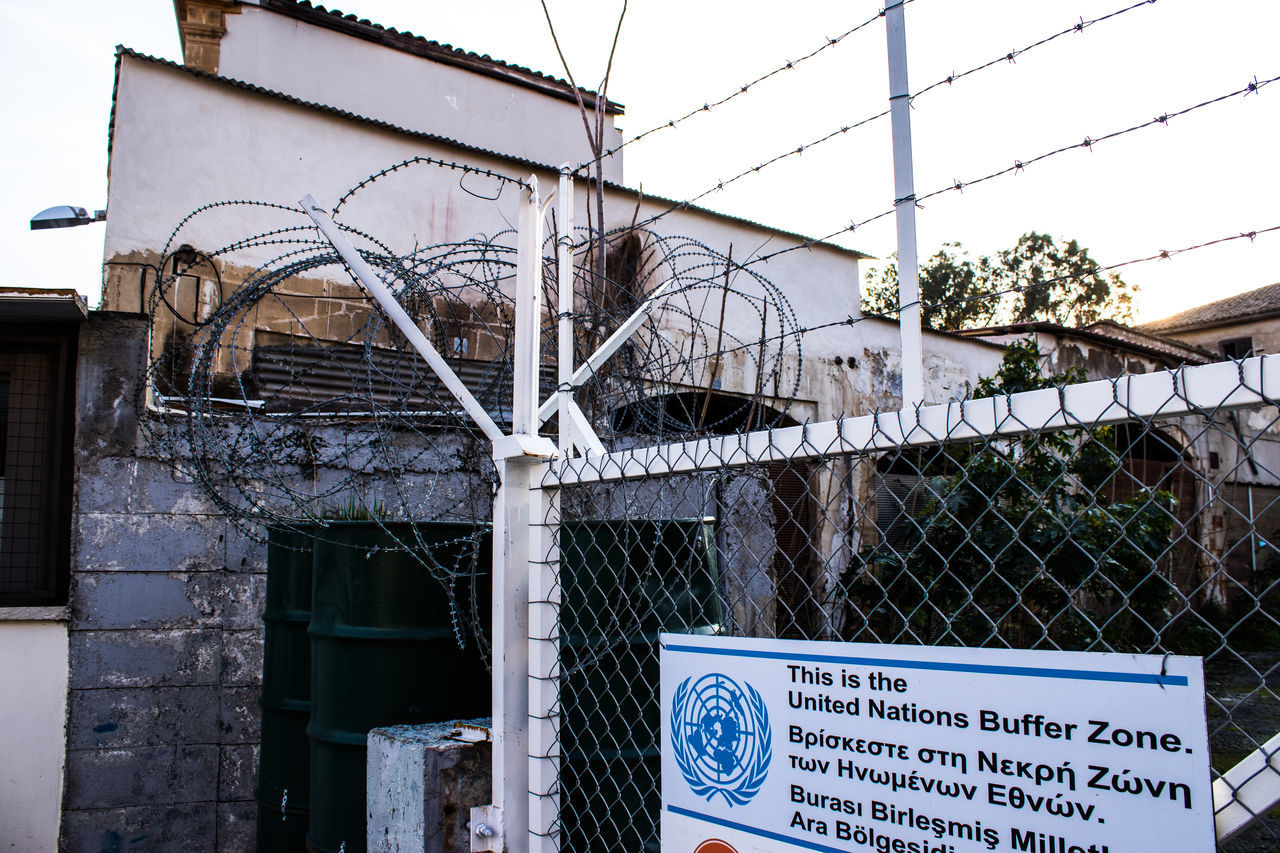 architecture, urban area, built structure, text, sign, communication, building exterior, fence, no people, western script, day, building, wire, sky, city, chainlink fence, security, outdoors, wire fencing, nature, street, protection, barbed wire, metal, information sign