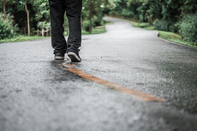 Low section of man walking on wet road