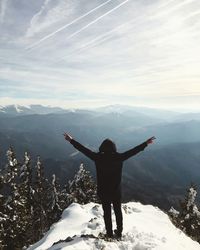 Rear view of man with arms outstretched standing on snow covered mountain