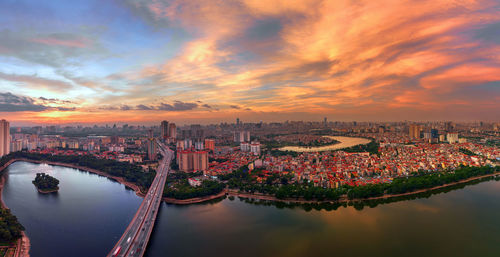 Aerial view of bridge over river and buildings against sky during sunset