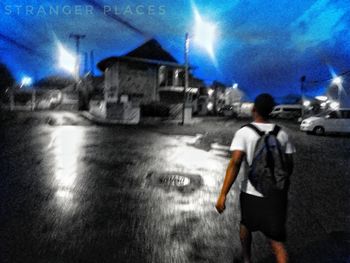 Rear view of man walking on illuminated road at night