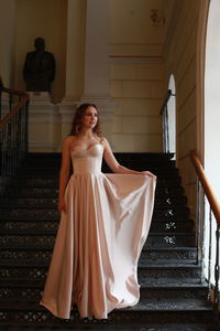 Smiling beautiful young woman wearing dress while standing on staircase