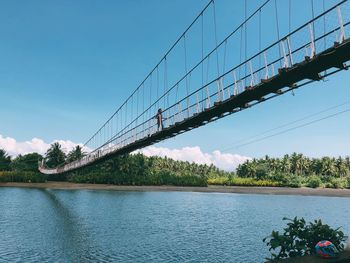 Low angle view of woman crossing river on footbridge against sky