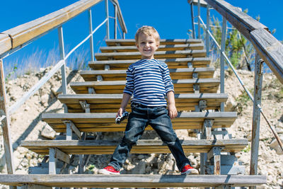 Portrait of smiling boy standing on staircase against sky