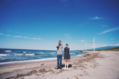 Rear view of woman standing at beach against blue sky