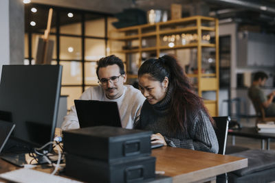 Smiling businesswoman working with male colleague on laptop in creative office