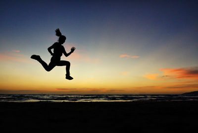 Silhouette man jumping on beach against sky during sunset