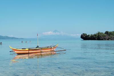 Boats moored on sea against clear blue sky