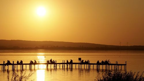 Silhouette people on lake against orange sky