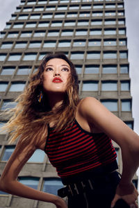 Low angle view of thoughtful woman bending against skyscraper