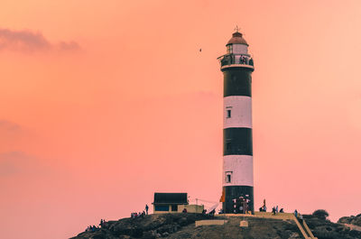 Low angle view of lighthouse by building against sky during sunset