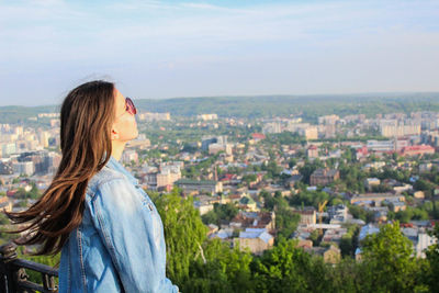 Young woman looking at cityscape against sky