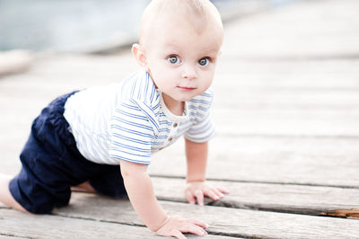 Cute baby boy 1 year old crawling on wooden pier outdoors. wearing striped clothes