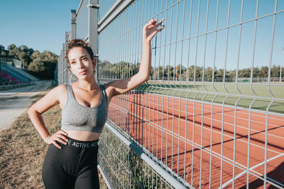 Young woman standing against chainlink fence