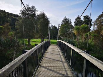 Footbridge amidst trees against sky