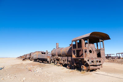 Abandoned train on desert against clear blue sky