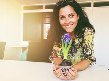 Happy young woman holding hyacinth flower pot while looking away at home