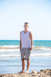 Full length portrait of young man standing at beach against clear sky