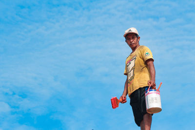 Low angle portrait of smiling man holding umbrella against sky