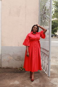 Portrait of happy young woman standing against red wall