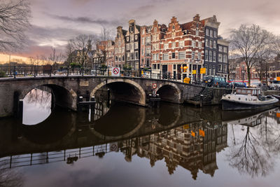 Bridge over river by buildings against sky in city