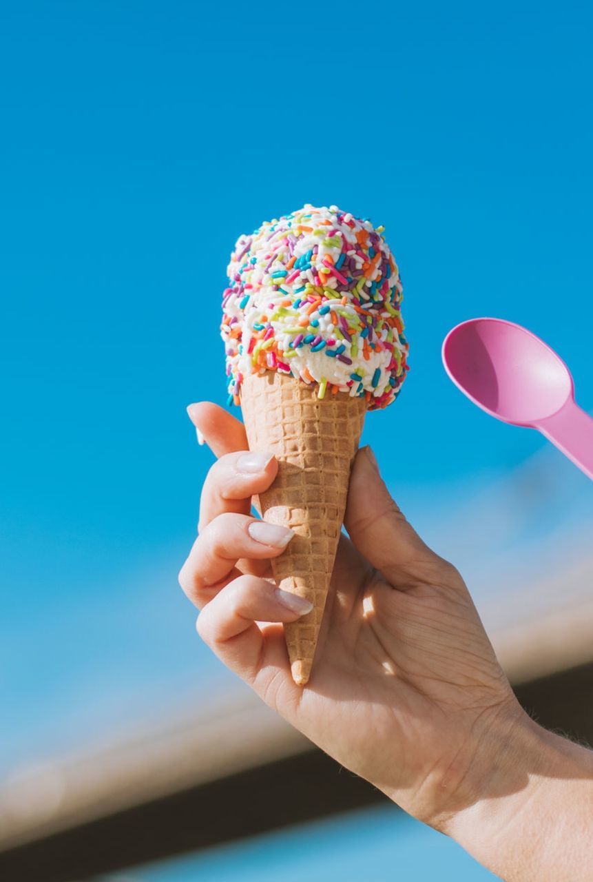 ice cream cone, sweet food, sweet, ice cream, frozen food, hand, frozen, cone, food and drink, dessert, holding, food, blue, dairy, temptation, finger, one person, unhealthy eating, summer, freshness, close-up, adult, sky, multi colored, nature, day