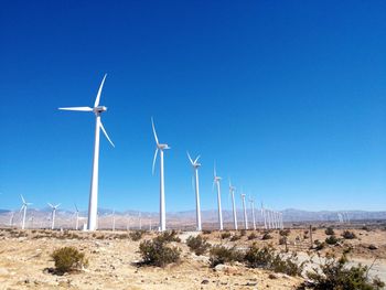 Wind turbines on land against clear blue sky