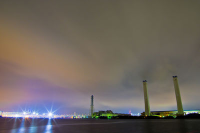 Illuminated factory by river against sky at night