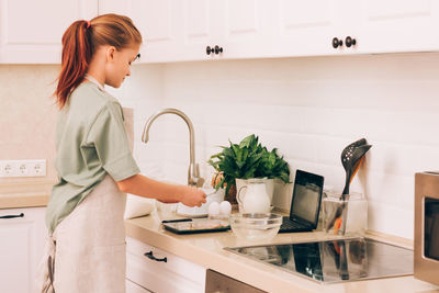 Side view of young woman standing in kitchen