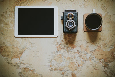 Directly above shot of digital tablet with vintage camera and coffee on world map