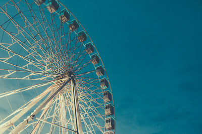 Low angle view of ferris wheel at amusement park against blue sky during sunset