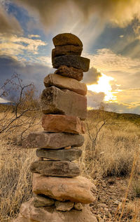 Stack of rocks on field against sky during sunset
