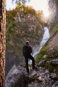 Rear view of man with backpack standing on rock looking at boka waterfall in slovenia during sunset 
