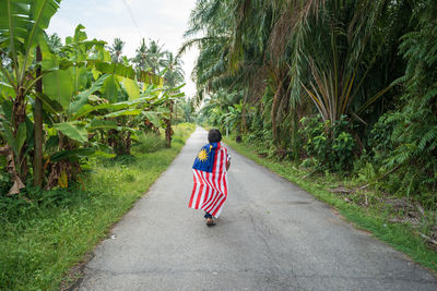 Rear view full length of boy with malaysian flag walking on road 