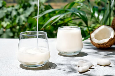 Coconut milk pouring in drinking glass on palm leaf background. vegetable milk, lactose free drink. 