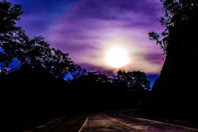 Road amidst silhouette trees against sky during sunset