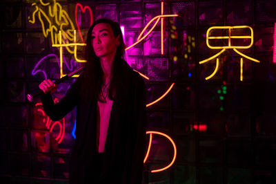 Portrait of young woman standing against graffiti at night