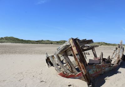 Shipwreck at sandy beach against blue sky