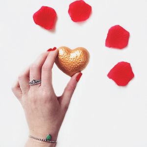 Cropped hand of woman holding heart shape chocolate over white background