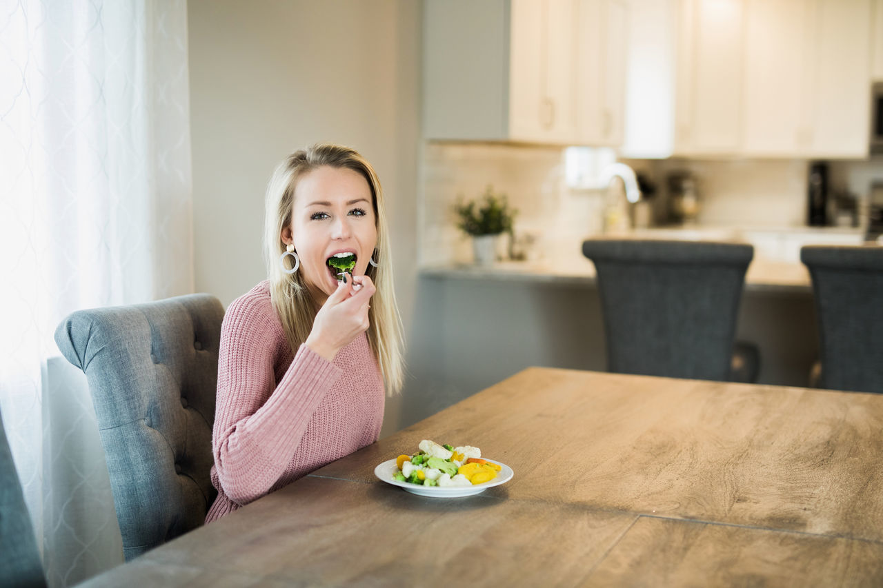 food, food and drink, eating, lifestyles, one person, sitting, indoors, front view, portrait, real people, home interior, table, casual clothing, wellbeing, looking at camera, healthy eating, young adult, freshness, leisure activity, mouth open